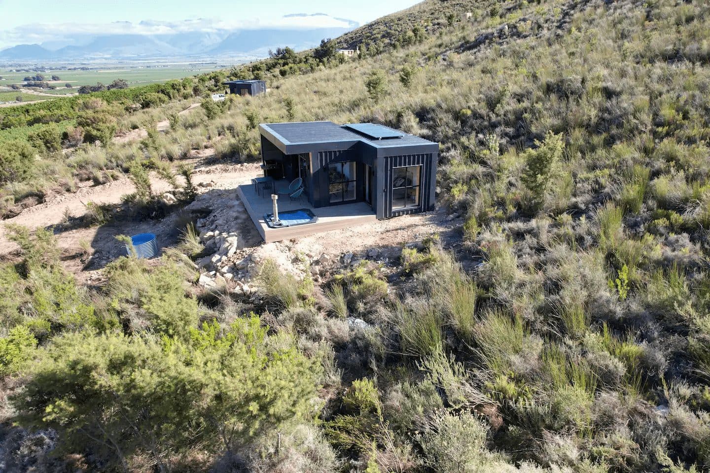 Better Days Cabin: Aerial black cabin on hillside, hot tub on deck, valley views
