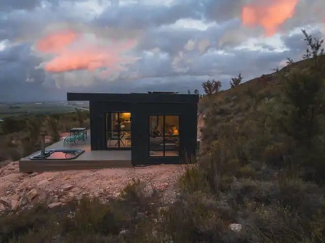 Better Days Cabin: Black cabin glowing at dusk, pink sunset clouds, hot tub on deck
