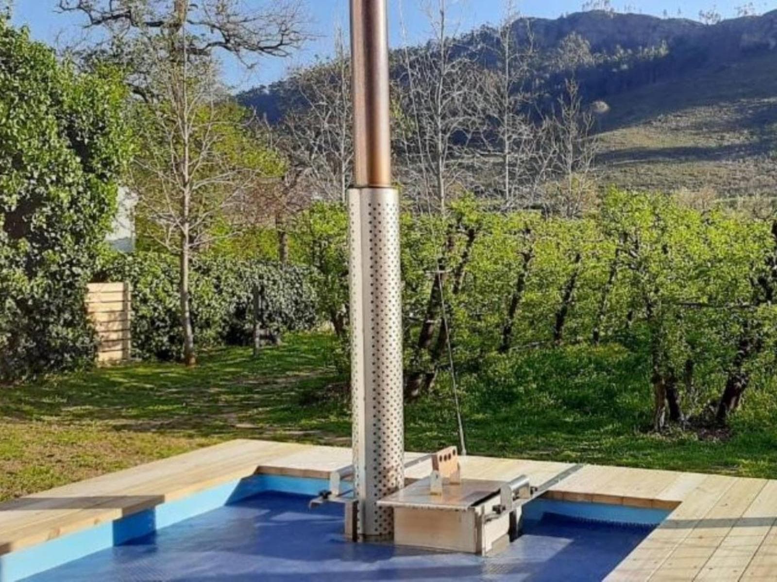 Gite Studio Franschhoek: Wood-fired hot tub on deck against orchard and mountain backdrop